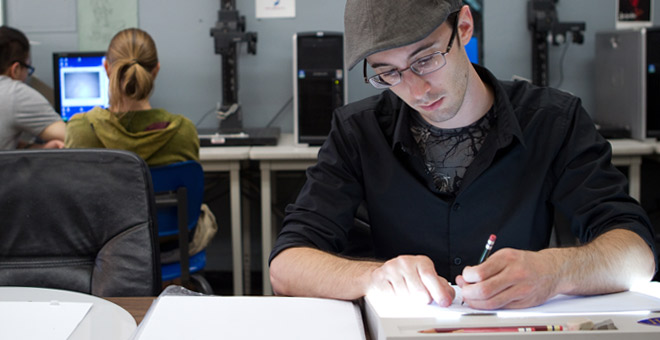 A student is working in a textbook, sitting at a desk.