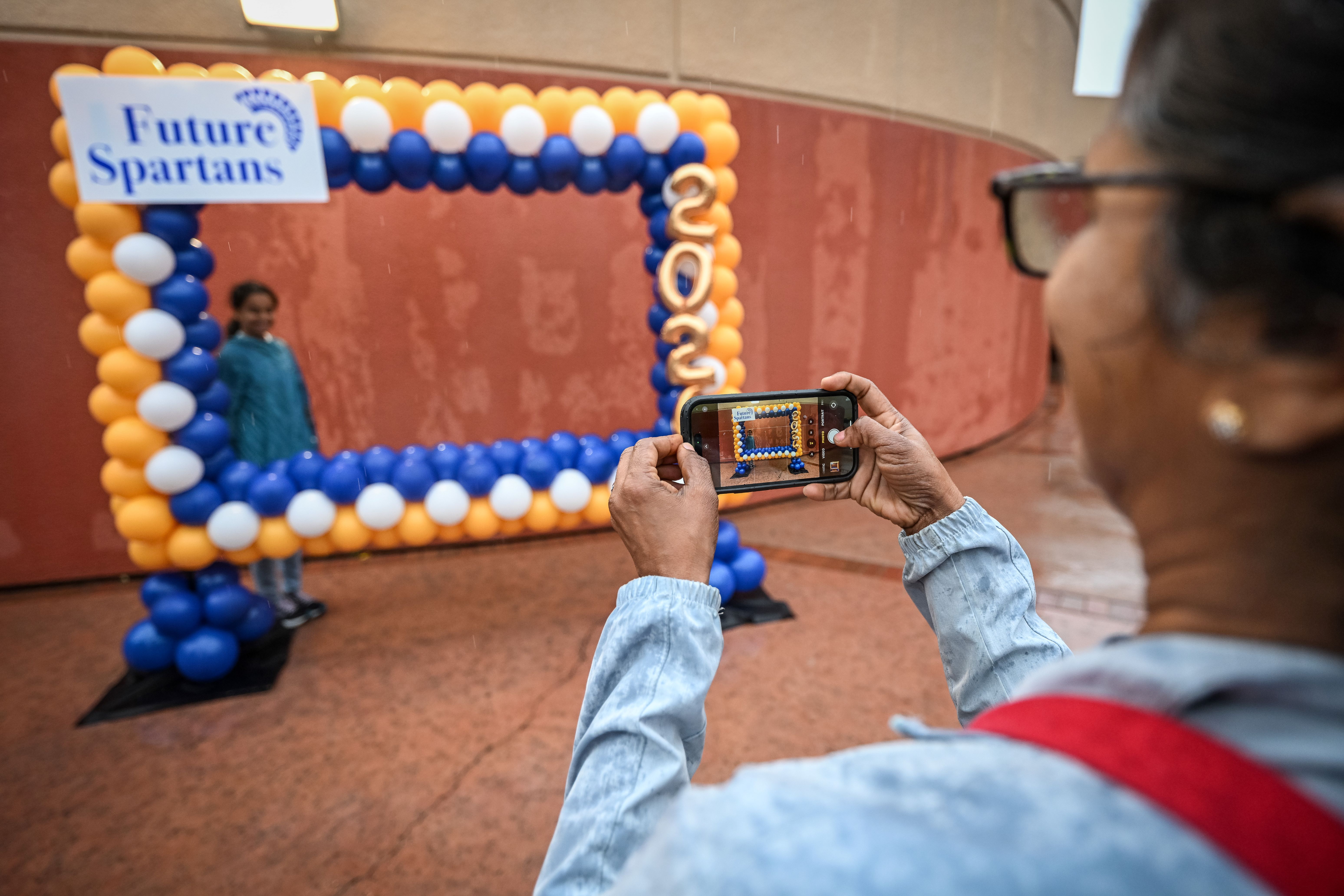 Parent taking a photo of their future Spartan behind a frame of yellow and blue balloons.